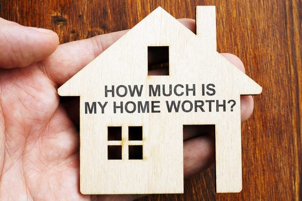 wooden cut out of a house with the question "how much is my home worth?" printed on it